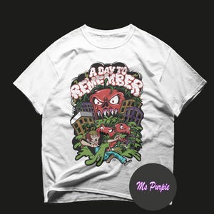 May include: A white short-sleeve t-shirt featuring a graphic print of a person running from monstrous red tomatoes in a city. The text A DAY TO REMEMBER is printed in a stylized font above the illustration. A small circular logo reads Ms Purpie.