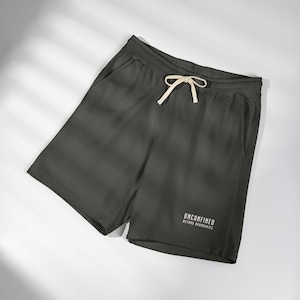 May include: Dark charcoal gray shorts featuring an elastic waistband with a cream-colored drawstring. The lower right leg displays the white text UNCONFINED BEYOND BOUNDARIES in a clean, sans-serif font. The shorts have two side pockets.