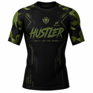 Puede incluir: Una camiseta de compresión negra de manga corta con mangas de camuflaje verde oliva. El frente presenta el texto HUSTLER, BUILT FOR THE GRIND y FIGHT GRIND DOMINATE, junto con un logotipo de casco espartano y la marca PEXTON en blanco y verde.