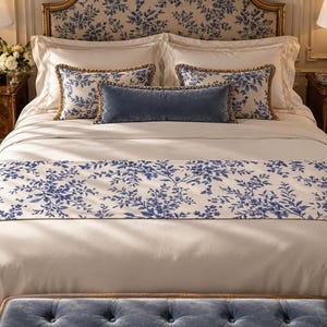 Puede incluir: Un juego de cama que incluye una funda nórdica color crema y un camino de cama a juego con estampado floral azul. La cama cuenta con dos almohadas grandes color crema, dos almohadas rectangulares con estampado floral azul y un cojín azul.