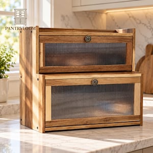 May include: A two-tier wooden bread box featuring a natural brown wood grain finish, two drop-down doors with fluted glass panels, and small circular metal knobs. The unit is rectangular with visible side screws and a sturdy frame construction.