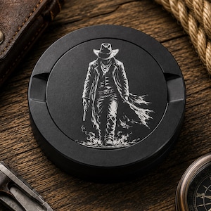 May include: A circular black metal ashtray featuring a white laser-engraved illustration of a cowboy wearing a wide-brimmed hat and a long duster coat, holding a revolver while walking forward with a stylized smoke or dust effect at the feet.