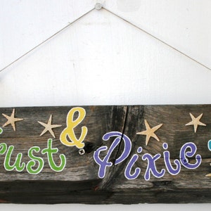 Puede incluir: Un letrero de madera rústico con las palabras "Faith Trust & Pixie Dust" pintadas en letras de colores. El letrero está decorado con pequeñas estrellas y cuentas.