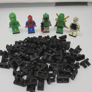 May include: Five plastic minifigures including a green character, a red and blue superhero, a green armoured figure with a blaster, a green ninja with gold swords, and a gold robot, positioned behind a large pile of small black plastic connectors.