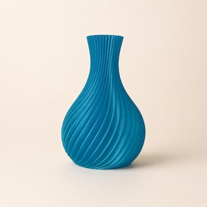 Può includere: Un vaso blu brillante con una distinta trama a coste a spirale. Il recipiente presenta una base ampia e arrotondata che si restringe verso l'alto in un collo stretto, mostrando un motivo verticale costante di creste su tutta la superficie.