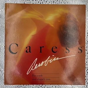 May include: A square advertisement with a warm, orange and red gradient background. The word "Caress" is printed in black, bold letters, with the word "Aerobin" in a cursive, white font. The text "For a soft and shapely you" is also visible.