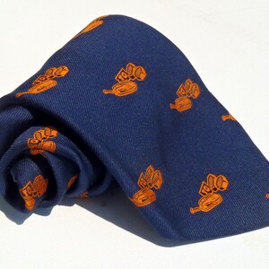 Może przedstawiać: Granatowy krawat z powtarzającym się wzorem pomarańczowych ciągników.
