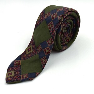 Peut inclure: Cravate vert olive roulée, ornée d'un motif répétitif de losanges bleu marine et bordeaux. La cravate est en tissu texturé et le motif est visible sur le rouleau.