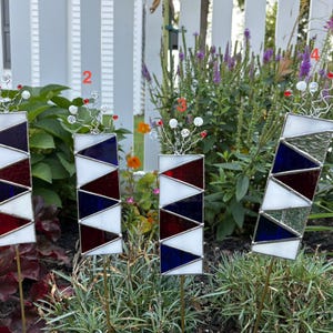 May include: Four rectangular stained glass garden stakes featuring geometric patterns of white, red, and blue triangles. Each stake is topped with silver wire accents and clear beads, numbered one through four in red text on the image.