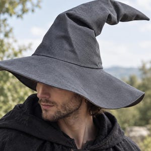 May include: A charcoal gray pointed hat with a wide, slightly drooping brim and a tall, curved crown. The hat is constructed from a textured fabric and features a distinct, slouchy silhouette that tapers to a soft, rounded point at the top.