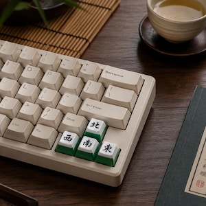 May include: A mechanical keyboard with off-white keycaps and a beige frame. Three keys in the bottom right corner feature green bases and white tops with black Chinese characters representing cardinal directions: North, South, West, and East.