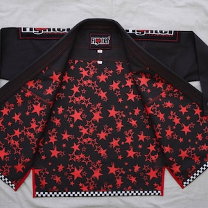 May include: A black martial arts gi jacket featuring a red star pattern on the interior lining. The garment displays the text Fighter Techniques on the shoulders and a Fighter logo on the inner neck label, with a black and white checkered trim.