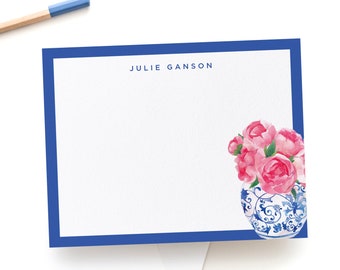 Pode incluir: Um vaso de porcelana azul e branco com flores cor-de-rosa, com o nome "JULIE GANSON" impresso acima do vaso. O vaso está sobre um fundo branco.