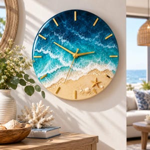 May include: A round wall clock featuring a resin ocean scene with deep blue and turquoise water, white foam waves, and a sandy beach shore. The clock has gold-colored hands and hour markers, with a small starfish and seashells on the sand.