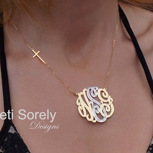 Puede incluir: Un collar de cadena dorada con un gran colgante redondo de plata y oro. El colgante presenta las letras "N.S.C." en escritura cursiva. El collar también presenta un pequeño dije de cruz dorada.