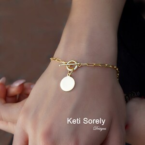 May include: Gold chain bracelet with a toggle clasp and a round pendant. The pendant is blank and can be personalized.