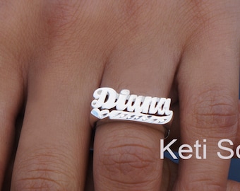 Puede incluir: Anillo de plata con el nombre "Diana" escrito en letras cursivas. El anillo se lleva en el dedo de una persona. La imagen incluye el texto "Ketti Sorely Designs".