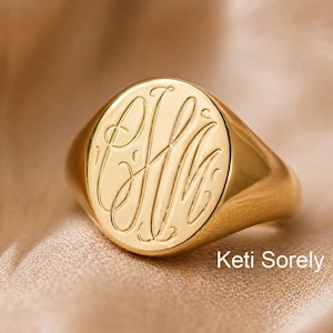 May include: A gold signet ring with an oval face, engraved with elegant initials. The ring has a polished finish and is set against a neutral background. The text "Keti Sorely" is visible at the bottom of the image.