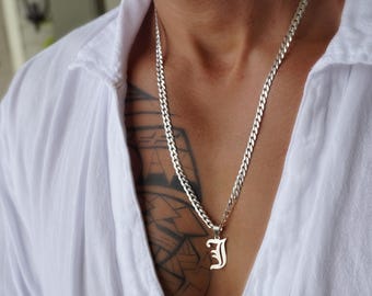 Puede incluir: Un collar de cadena plateada con un colgante con la letra "J" en fuente inglesa antigua. El collar se lleva sobre una camisa blanca abotonada.