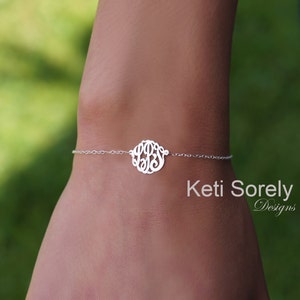 Könnte beinhalten: Ein silbernes Kettenarmband mit einem runden Monogramm-Anhänger. Der Anhänger zeigt die Buchstaben "LBS" in einer kursivschriftlichen Schriftart. Das Armband befindet sich am Handgelenk einer Person.