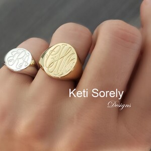 K&ouml;nnte beinhalten: Zwei gravierte Siegelringe, einer aus Gold und einer aus Silber, die jeweils elegante Monogramm-Initialen zeigen. Der goldene Ring ist gr&ouml;&szlig;er und auff&auml;lliger, w&auml;hrend der silberne Ring kleiner ist und einen wei&szlig;en Hintergrund hat. Die Ringe werden an einer Hand getragen.