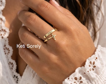 Puede incluir: Un anillo dorado con un colgante de cruz y el nombre "Vivvi" grabado en la banda. El anillo se lleva en un dedo. La imagen también muestra el texto "Keti Sorely".
