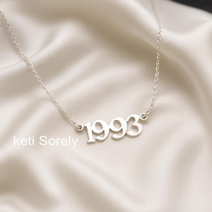 May include: A silver necklace with a pendant that says "1993".