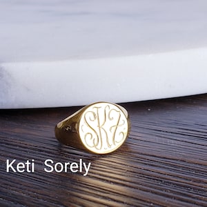 Puede incluir: Un anillo de sello de oro con una parte superior redonda grabada con las iniciales "SKZ".