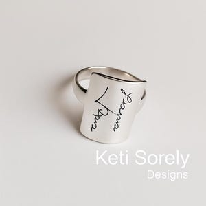Puede incluir: Anillo de plata con una banda rectangular inclinada grabada con la palabra "remarkable" en cursiva.