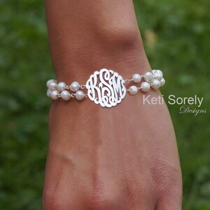 Peut inclure: Un bracelet en argent avec deux rangées de perles blanches. Le bracelet comporte un monogramme circulaire au centre avec les initiales KSM. Le bracelet est porté sur un poignet sur un fond vert flou.