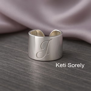 Puede incluir: Anillo de plata con una letra "J" en cursiva grabada en la parte delantera. El anillo es grueso y tiene una forma redondeada.