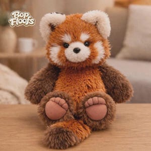 May include: A plush red panda toy with soft, shaggy fur in shades of reddish-brown and dark brown, featuring white facial markings, black eyes, a small black nose, and rounded ears. The text Bop Floofs is visible in the upper left corner.