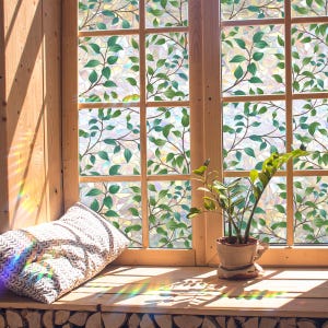 Könnte beinhalten: Eine Fensterfolie mit einem sich wiederholenden Muster aus grünen Blättern auf einem durchscheinenden, irisierenden Hintergrund. Die Folie ist auf einem Holzfensterrahmen angebracht und erzeugt einen Buntglaseffekt mit Lichtreflexen.