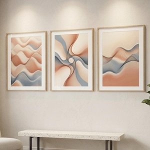 May include: A set of three framed wall art prints featuring abstract line art. Each print displays flowing, wave-like patterns in shades of peach, beige, and slate blue, contained within light-colored wooden frames and white matting.