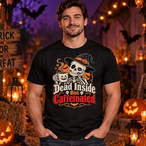 May include: A black short-sleeve t-shirt featuring a graphic of a skeleton wearing a witch hat and holding a coffee mug. The text reads Dead Inside But Caffeinated, accompanied by small skull icons, bats, and an orange circular background element.