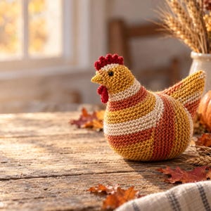 May include: A hand-knitted chicken figurine featuring horizontal stripes in shades of mustard yellow, burnt orange, and cream. The chicken has a bright red comb and wattle, a small yellow beak, and a rounded body shape crafted from yarn.