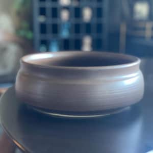 May include: A brown ceramic bowl with a smooth, slightly textured surface. The bowl has a rounded shape and a wide rim.