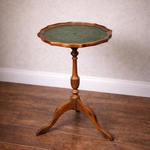 May include: A small, antique wooden side table with a scalloped edge and a green felt top. The table has a pedestal base with three curved legs. The wood has a warm, natural finish.