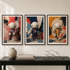 Peut inclure: Trois impressions d'art mural encadrées représentant des personnages de dessin animé stylisés avec de grandes têtes et des yeux ronds. Chaque personnage porte une combinaison avec un emblème d'éclair. Les fonds sont composés de taches de peinture abstraites.