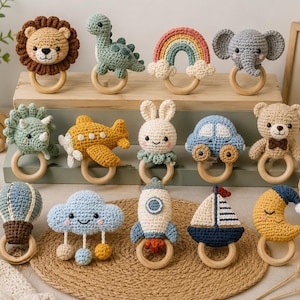 May include: A collection of fourteen crochet rattles featuring various shapes including a lion, dinosaur, rainbow, elephant, triceratops, aeroplane, rabbit, car, bear, hot air balloon, cloud, rocket, sailboat, and moon, each attached to a wooden ring.