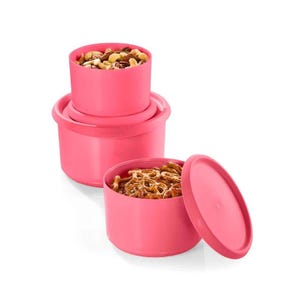 May include: Three bright pink round plastic food storage containers with lids. One container is stacked on top of another, while the third sits in front with its lid removed, revealing a portion of brown twisted pretzels inside.