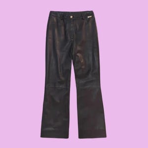 May include: Black leather pants with a flared leg design. The pants have a button and zipper closure at the waist, with a small gold-colored detail near the button. The pants are displayed against a light purple background.