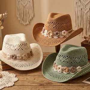 May include: Three cowboy hats in cream, tan, and sage green, each crafted from woven straw with a wide brim and a pinched crown. A band of crocheted lace and small, multi-toned fabric flowers encircles the base of each hat crown.