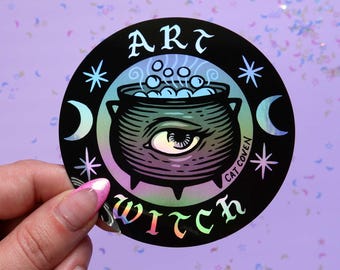 May include: A black and iridescent sticker with a cauldron, stars, and the text "Art Witch" and "Cat Coven".