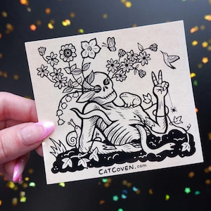 May include: Black and white illustration of a skeletal figure with flowers growing from its head. The figure is sitting with its legs crossed and has a hand raised in a peace sign. The illustration is on a beige background with the text "CATCOVEN.com" at the bottom.