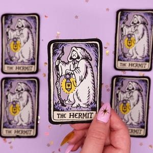 May include: Rectangular tarot card patches featuring "The Hermit" in a black border. The design shows a robed figure holding a lantern and staff, with a purple and white color scheme. The text "THE HERMIT" is at the bottom.