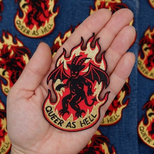 May include: Embroidered patch featuring a red devil figure with black wings and a smiling face, surrounded by flames. The patch has the text "QUEER AS HELL" in a circular design, with gold and black accents.