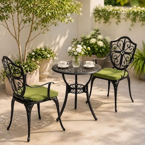 May include: A bistro set consisting of a round black metal table and two matching chairs with intricate scrollwork backrests. Each chair features a solid lime green seat cushion. A clear glass vase with white flowers sits on the table.