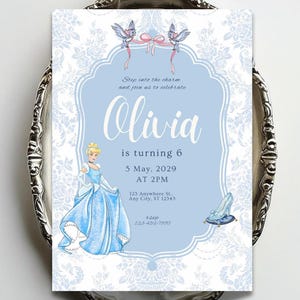 May include: A rectangular invitation card featuring a light blue background with a white floral damask border. It displays a cartoon princess in a blue gown, two blue birds with a pink ribbon, and a glass slipper on a blue cushion. Text reads: Step into the charm and join us to celebrate Olivia is turning 6, 5 May, 2029 AT 2PM, 123 Anywhere St., Any City, ST 12345, rsvp 123-456-7810.