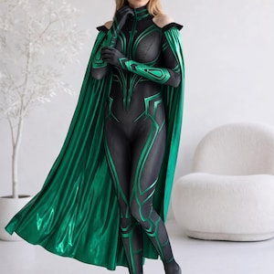 May include: A black and green full-body jumpsuit featuring a textured mesh pattern, long sleeves with cut-out shoulders, and a high collar. The garment includes a long, metallic green cape attached at the shoulders and matching green gloves.